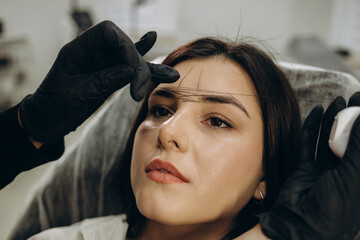 Fototapeta premium The make-up artist plucks eyebrows with a thread close-up. Women's cosmetology in the beauty salon.