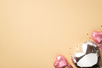 Valentine's Day atmosphere concept. Top view photo of heart shaped metallic balloons and sparkling confetti on isolated pastel beige background with copyspace