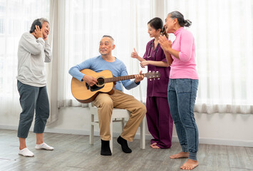 Selective focus senior man happy playing acoustic guitar with friends. Elderly male musician sitting at party has fun with cheerful family singing together. Leisure activity of asian grandfather.