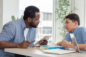 African American teacher and child student studying in classroom. Multiracial male tutor teaching homework lesson to boy pupil in class. Schoolboy back to school and learning with multicultural person