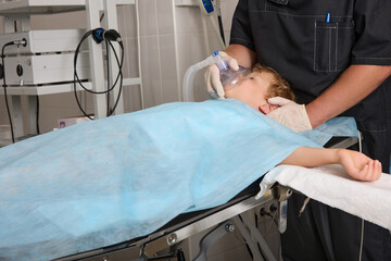 Small child fell asleep under anesthesia for surgery. An anesthesiologist in a black uniform used child anesthesia for the boy through a ventilation mask to perform a surgical procedure