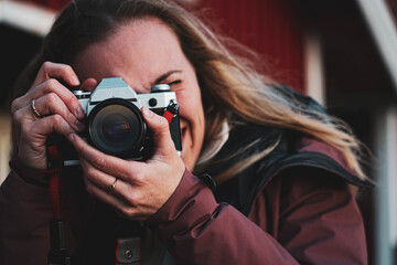 Blond woman takes a photo. Girl with long fair hair focuses with an analog camera. Inspiring young creative artist making photo with vintage retro camera.