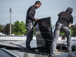 Male team engineers installing stand-alone solar photovoltaic panel system. Electricians mounting blue solar module on roof of company. Alternative energy concept