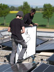 Male team engineers installing stand-alone solar photovoltaic panel system. Electricians mounting blue solar module on roof of company. Alternative energy concept