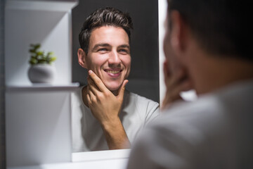 Portrait of man looking himself in a mirror while standing in bathroom.