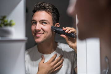 Man shaving  beard while looking himself in the mirror.