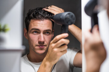 Man using hair dryer while looking himself in the mirror