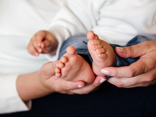 The feet and hands of a baby in the hands of his/her mother. Parenting, family life and mother love.