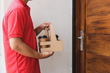 Cropped shot of a male courier in red uniform delivering coffee cups to customer in front of the house