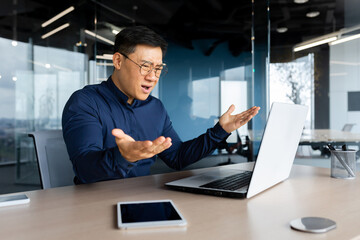 Angry and upset asian businessman, man working with laptop unhappy with result achievement, man inside office disappointed.