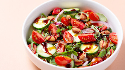 Healthy salad with tomato, cucumber, greens and nuts on light background