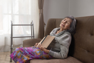 Elderly asian woman snooze while read a book on a sofa.