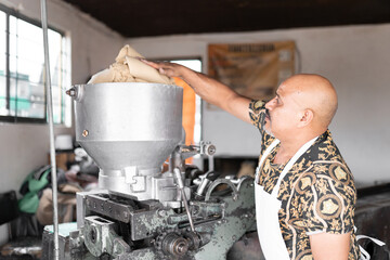 An adult tortilla maker is dropping some corn dough into the nixtamall mill in Mexico