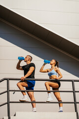 Urban sporty couple drinking water after training on a sunny day. They are taking a break