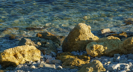 Large yellow rocks against the backdrop of the blue sea at sunset. Sea stones and rocks of different sizes and texture on beach and under water of Black Sea coast as nature background.