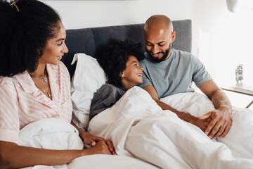 Obraz premium Happy black family with little boy smiling while lying together in bed