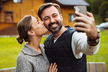 Smiling couple taking selfie and kissing while standing outdoors