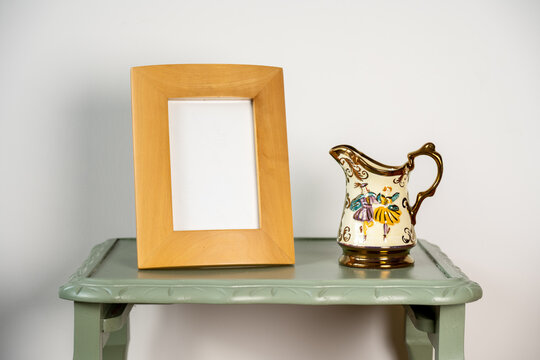 beech blank photo picture frame mock up with retro antique pouring jug on a green wooden table plain background