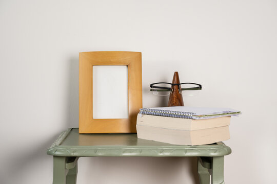 empty picture frame mock up with soft backed books wooden glasses stand on green table plain background