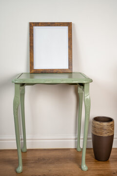 picture photo frame mock up on a green table against a clean wall background and wooden floor with ceramic vase