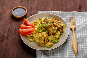 Thai chicken rice garnished with green onions on a wooden table next to a soy sauce napkin and a wooden fork.