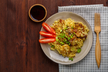 Thai chicken rice garnished with green onions on a wooden table next to soy sauce napkin and wooden fork.copy space
