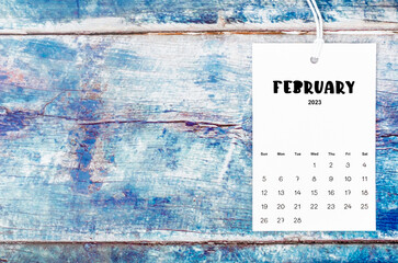 The February 2023 calendar page hanged with white rope  on old blue wooden background.