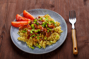 Rice chicken in teriyaki sauce garnished with green onions on a wooden table next to soy sauce next to a fork.
