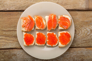 Toasts with red caviar and salted trout and butter on a plate on a wooden table.