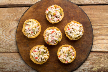 Salad in tartlets with shrimps and pineapple on a round wooden board.