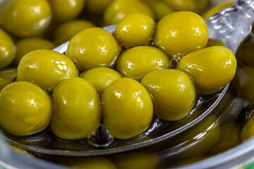 Spoon holding marinated sweet green peas in metal can container close up.