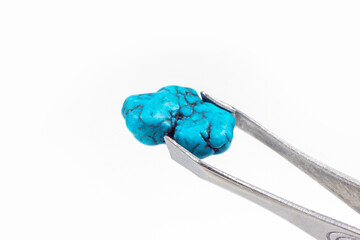 Bright light blue Turquoise crystal gem in the pincers on light background close up with copy space.