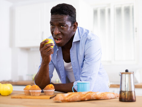 African American Man Eating Apples In Kitchen During Breakfast