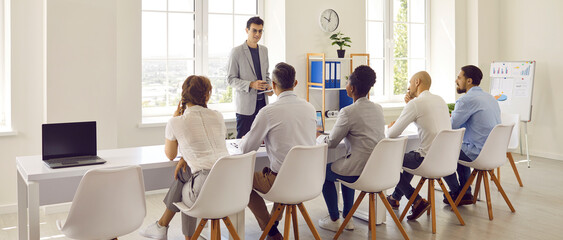 Man speaking in front of his colleagues discusses business matters with them during work meeting....