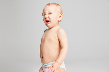 Funny cute toddler boy, baby in diaper having fun isolated over grey studio background. Concept of...