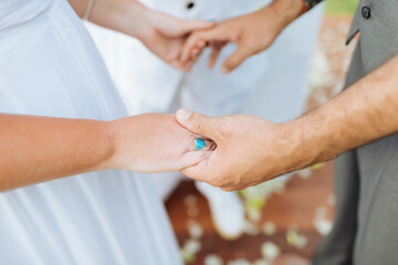 A picture of the bride and groom holding hands at the wedding ceremony. The bride wore a beautiful blue engagement ring at one place. There was a pastor standing as a witness.