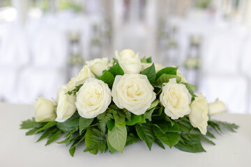 A large bouquet of many white roses Surrounded by green leaves on the table at a celebration somewhere, it looks beautiful and catches the eye.