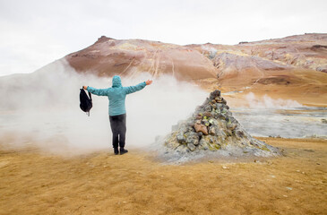 Woman tourist in Hverir , Iceland  geothermal area at the Namafjall volcanic mountain. Standing in natural steam vent inside smelly vapor. Hverir also known as Namafjall or Namaskard. - Powered by Adobe