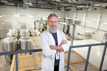 Confident brewer posing for the camera against beer fermentation tanks