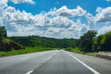 cars on the road in the countryside surrounded by trees and a beautiful cloudy and blue sky