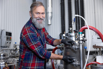 Man in plaid shirt working at the brewery and looking contented