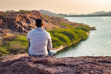 isolated young man sitting at mountain top with lake view from flat angle