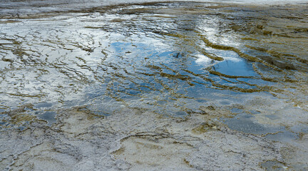 Reflection on waters at Yellowstone National Park shows the blue sky with white clouds. This is a ground closeup showing natural rock formations.