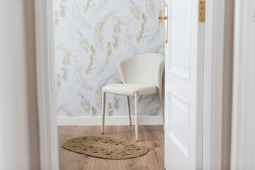Classic white chair in a bedroom with a natural wood floor, feathered wallpaper and a wicker rug, white doors