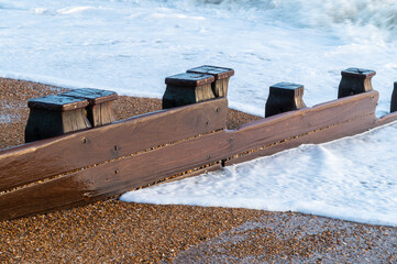 A beach groyne on the beach at Bexhill-on-Sea with waves and foam flowing over the shingle