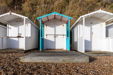 Three white wooden beach huts at Bexhill-on-Sea on a sunny day