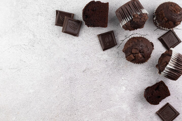 Chocolate muffins and pieces of chocolate on a gray background.