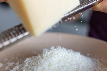 close-up of grater with parmesan cheese; person grates cheese on grater on a table.