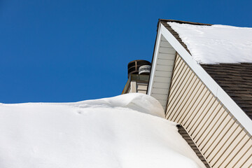 Snow drift on roof of house after winter storm. Roof damage, snow removal, home maintenance and repair concept.