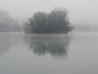 îlot sur lac dans la brume à l'aube et son reflet dans l'eau